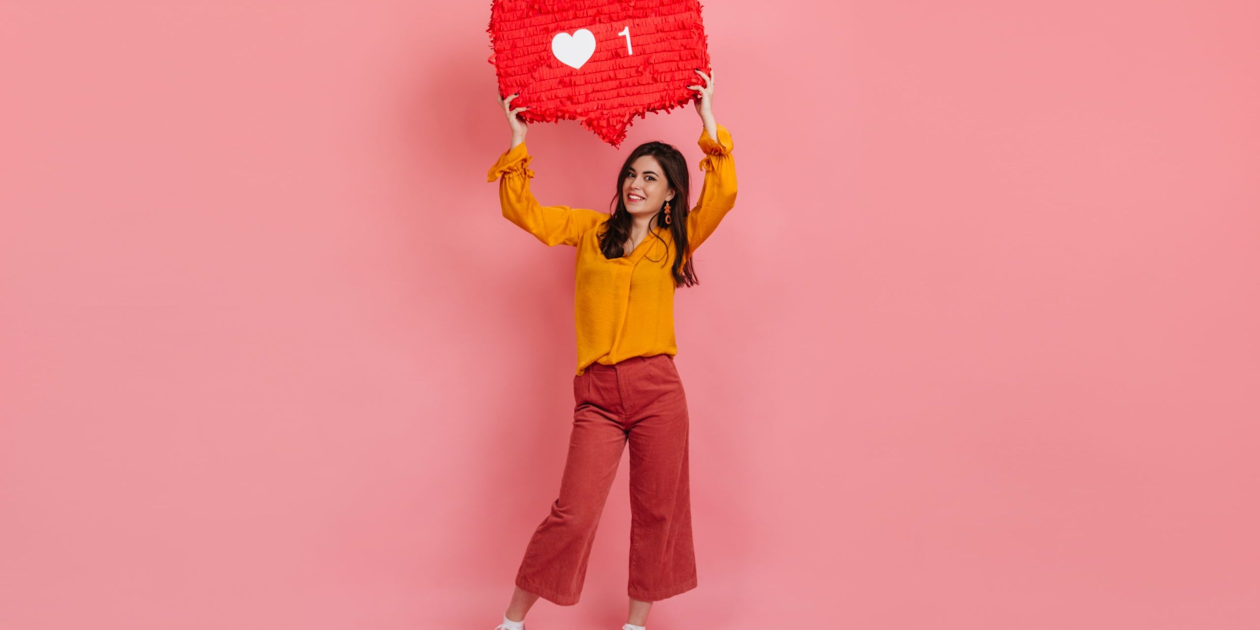 Full-length portrait of cheerful girl in culottes and yellow blouse holding «like» instagram sign.
